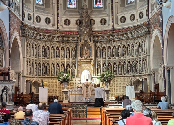 A priest celebrating Mass at a carved high altar, with a congregation in the pews