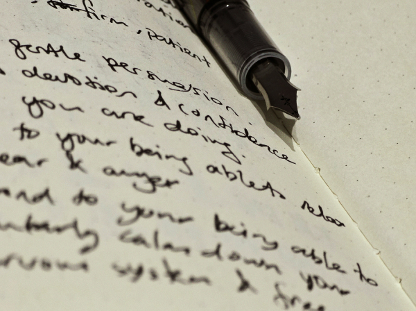 Handwriting in ink on paper, with a fountain pen resting on the page